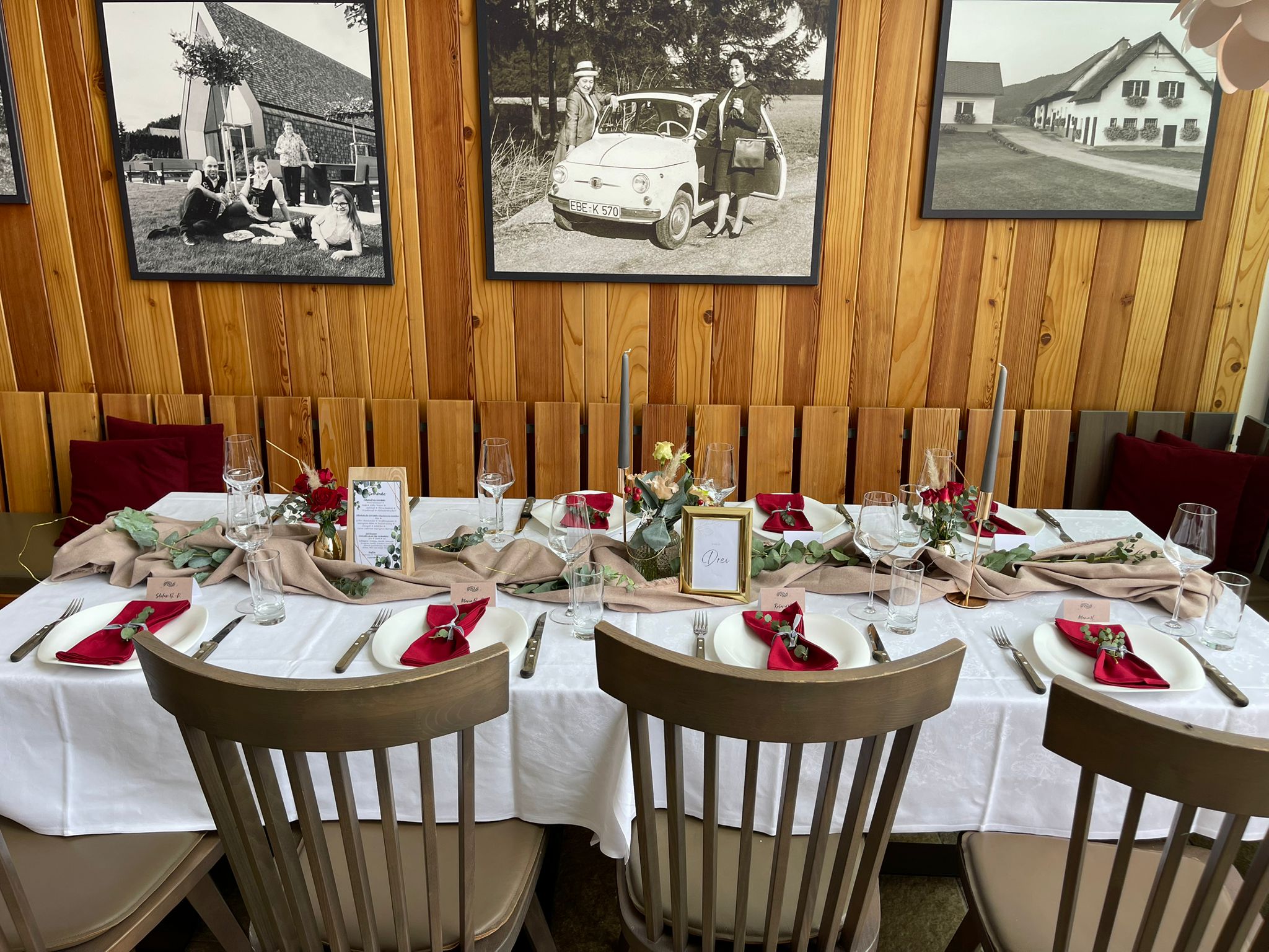 Festlich gedeckter langer Tisch im Innenraum mit roter Serviettendeko und historischen Fotos an der Wand.